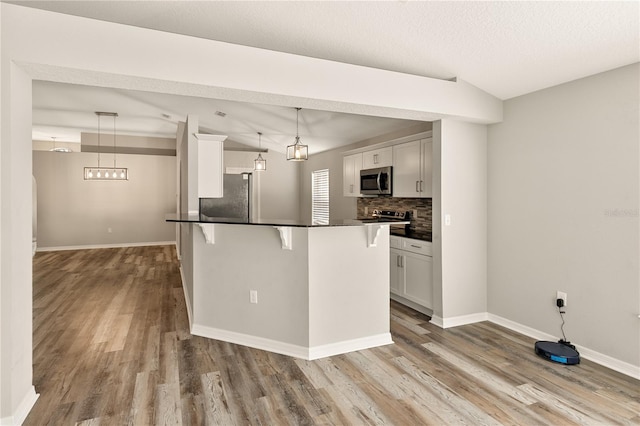 kitchen with white cabinets, hardwood / wood-style flooring, pendant lighting, and appliances with stainless steel finishes