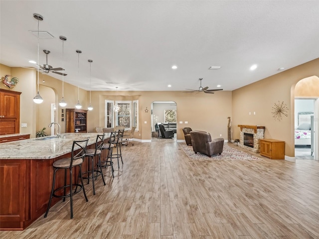 kitchen featuring a kitchen breakfast bar, light stone counters, light hardwood / wood-style floors, a stone fireplace, and hanging light fixtures