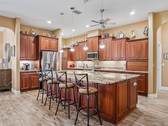 kitchen featuring light hardwood / wood-style floors, an island with sink, hanging light fixtures, and appliances with stainless steel finishes