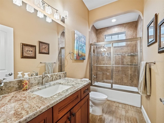 full bathroom with hardwood / wood-style floors, vanity, toilet, and bath / shower combo with glass door