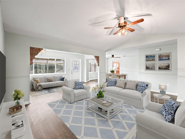 living room with a textured ceiling, light wood-type flooring, ceiling fan, and lofted ceiling