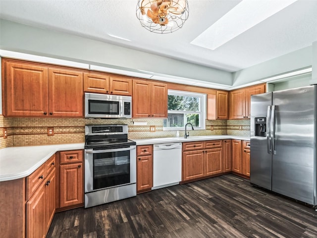 kitchen with sink, a skylight, dark hardwood / wood-style floors, decorative backsplash, and appliances with stainless steel finishes