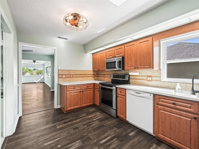 kitchen with appliances with stainless steel finishes, backsplash, a textured ceiling, ceiling fan, and dark hardwood / wood-style floors