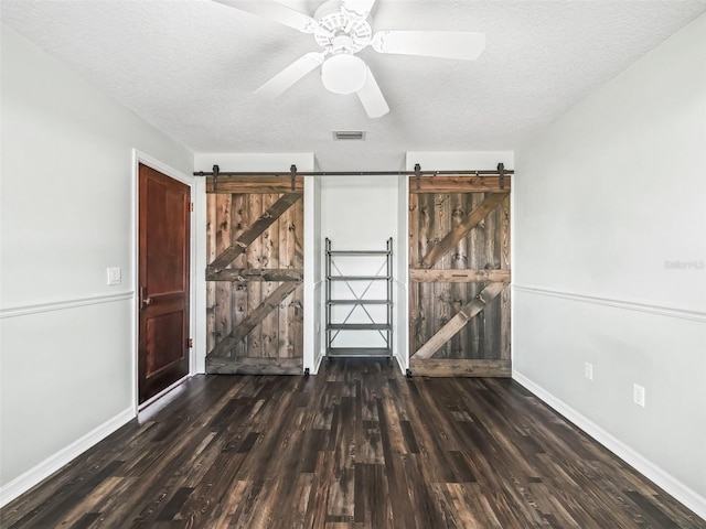 unfurnished bedroom featuring ceiling fan, a barn door, dark hardwood / wood-style flooring, and a textured ceiling