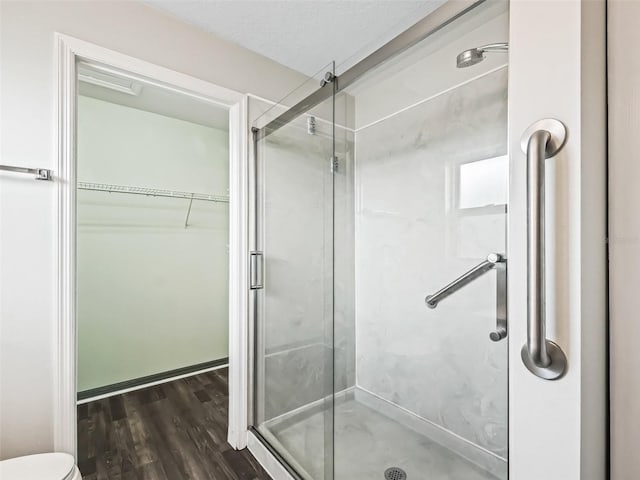 bathroom with toilet, a walk in closet, a stall shower, and wood finished floors