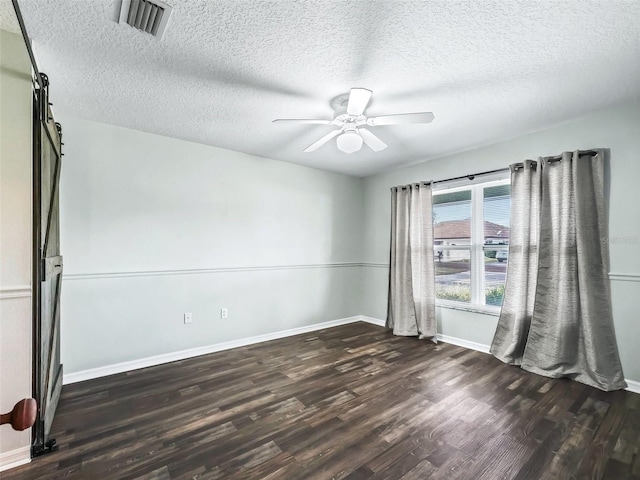 empty room featuring dark wood finished floors, a barn door, baseboards, visible vents, and a ceiling fan