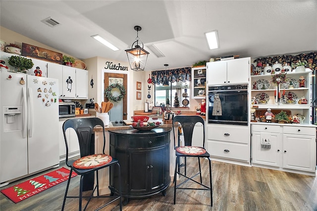 kitchen featuring white cabinets, black oven, white fridge with ice dispenser, and hanging light fixtures