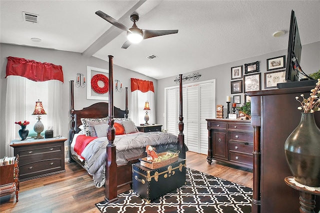 bedroom with a textured ceiling, ceiling fan, hardwood / wood-style floors, vaulted ceiling with beams, and a closet