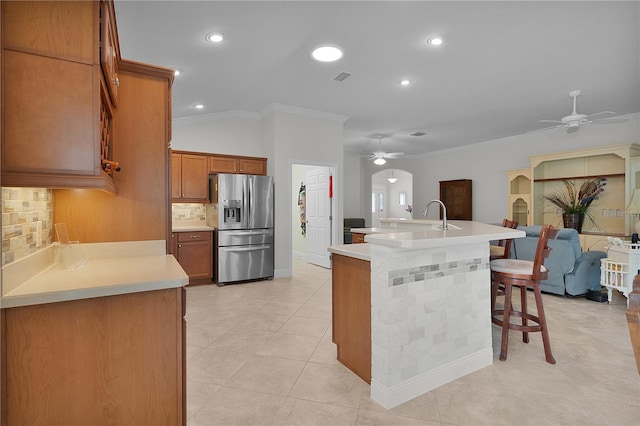 kitchen featuring a kitchen breakfast bar, stainless steel refrigerator with ice dispenser, crown molding, an island with sink, and decorative backsplash