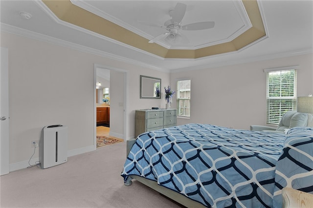 carpeted bedroom with a tray ceiling, connected bathroom, ceiling fan, and ornamental molding