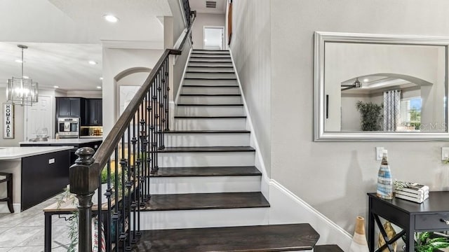 stairs with crown molding and ceiling fan with notable chandelier