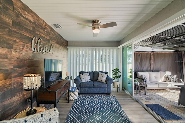 living room with light wood-type flooring, ceiling fan, and wood walls