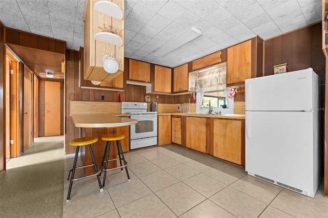 kitchen featuring kitchen peninsula, white appliances, a breakfast bar area, and wood walls