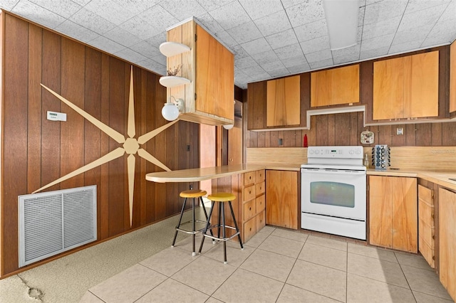 kitchen with light tile patterned flooring, a kitchen breakfast bar, white range with electric cooktop, and wood walls