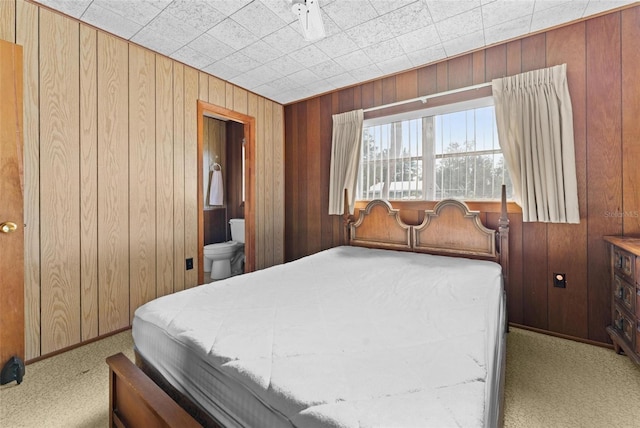 carpeted bedroom featuring connected bathroom and wood walls