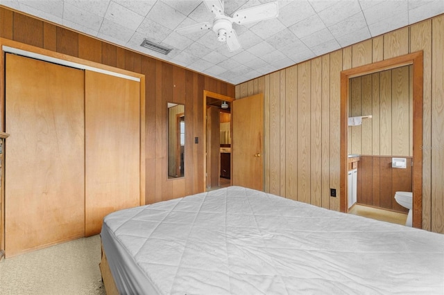 bedroom with a closet, light colored carpet, ceiling fan, and wood walls