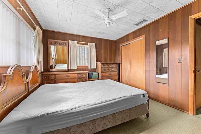 carpeted bedroom featuring ceiling fan, wood walls, and a closet