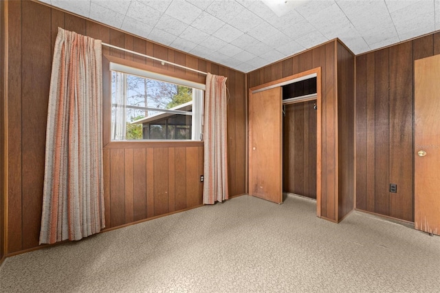 unfurnished bedroom with light carpet, wooden walls, and a closet