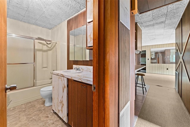 full bathroom featuring wooden walls, toilet, vanity, and combined bath / shower with glass door