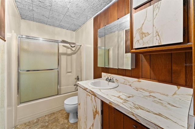 full bathroom featuring vanity, toilet, bath / shower combo with glass door, and wooden walls