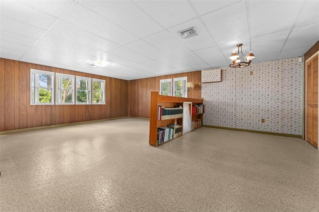 basement featuring a paneled ceiling, wood walls, and an inviting chandelier