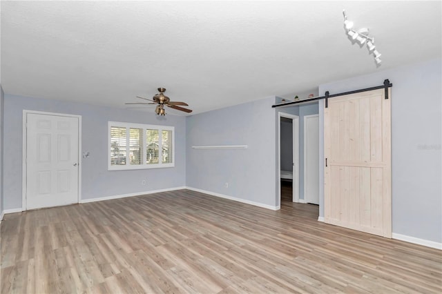 unfurnished living room featuring ceiling fan, a barn door, light hardwood / wood-style flooring, track lighting, and a textured ceiling