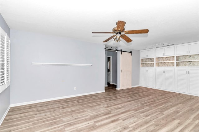 unfurnished bedroom featuring ceiling fan, a barn door, a closet, and light hardwood / wood-style flooring