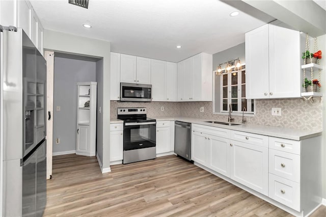 kitchen with white cabinetry, stainless steel appliances, decorative backsplash, sink, and light hardwood / wood-style flooring