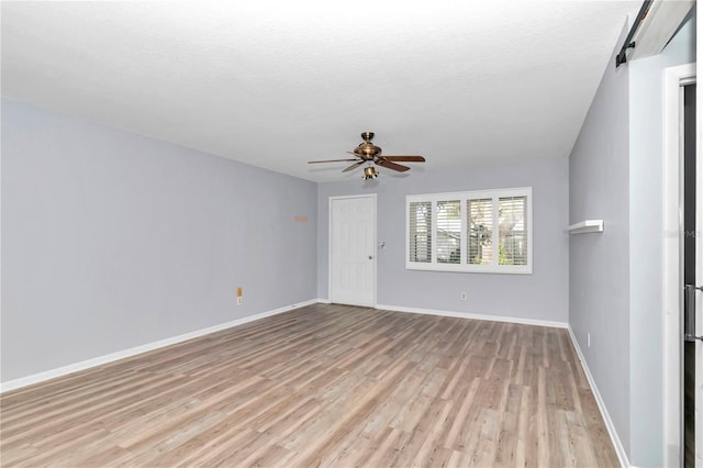 spare room featuring ceiling fan, a textured ceiling, a barn door, and light wood-type flooring