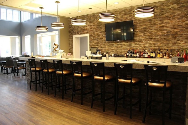 bar with dark wood-type flooring, a high ceiling, and hanging light fixtures