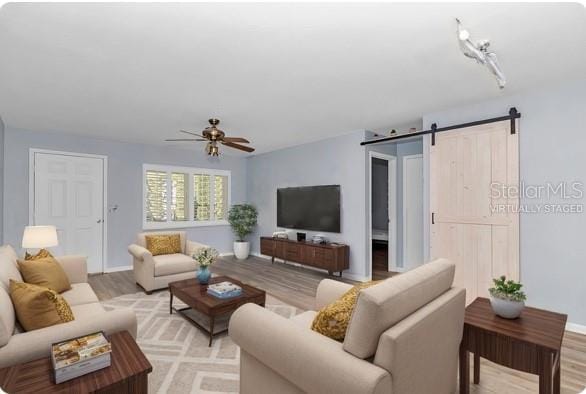 living room featuring light hardwood / wood-style floors, ceiling fan, and a barn door