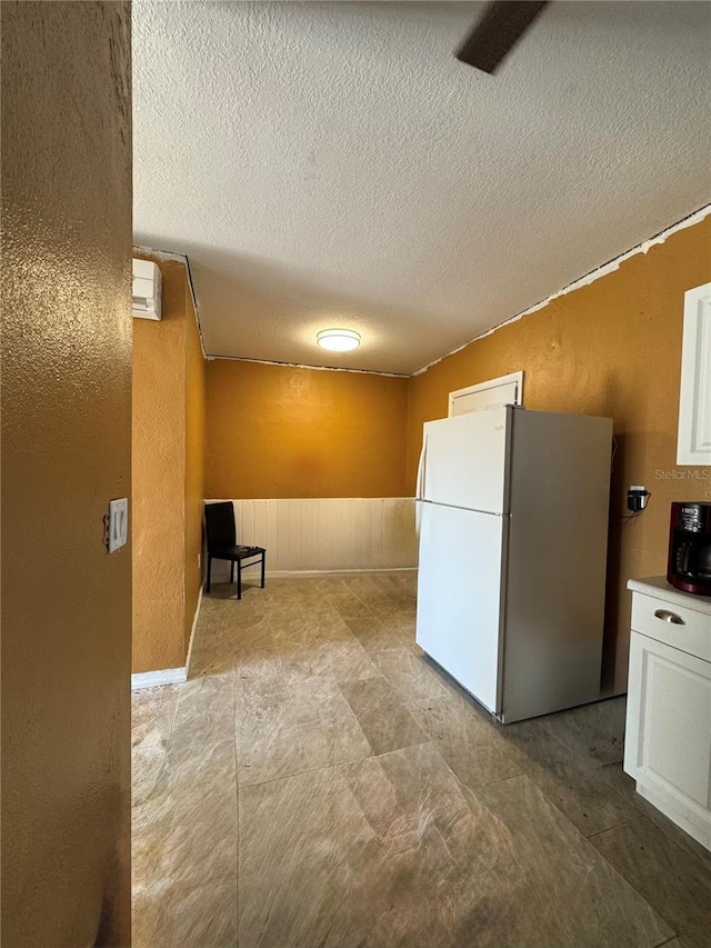 kitchen featuring white refrigerator, white cabinetry, and a textured ceiling