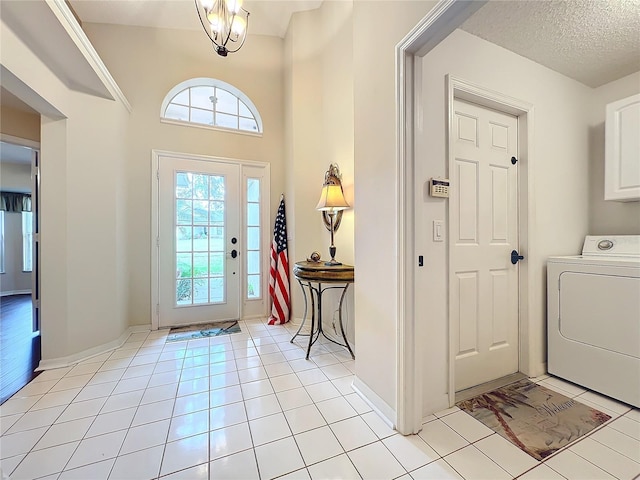 foyer entrance with a towering ceiling, a textured ceiling, light tile patterned floors, an inviting chandelier, and washer / clothes dryer