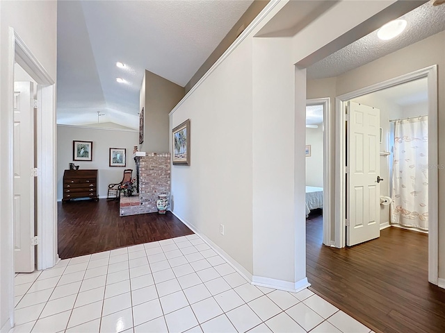 hall with a textured ceiling, lofted ceiling, and light wood-type flooring