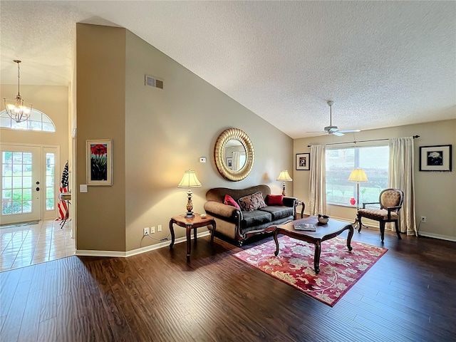 living room featuring ceiling fan with notable chandelier, a healthy amount of sunlight, a textured ceiling, and dark wood-type flooring