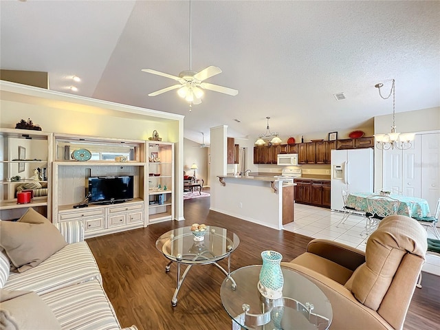 living room with a textured ceiling, ceiling fan with notable chandelier, light hardwood / wood-style flooring, and vaulted ceiling