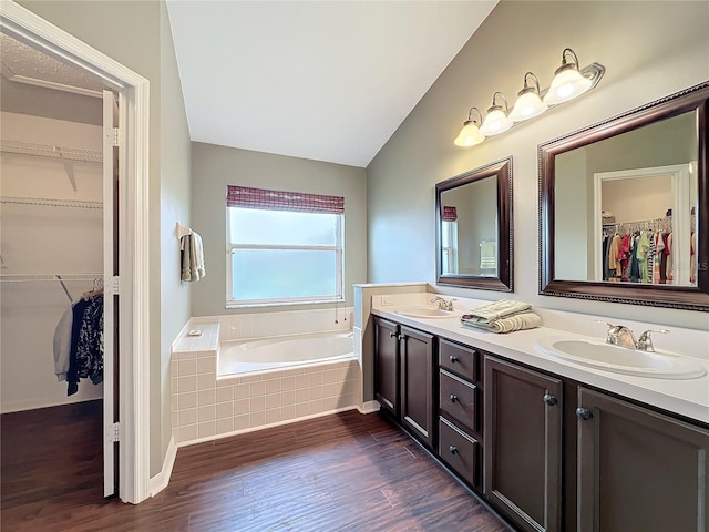 bathroom with hardwood / wood-style floors, vanity, a relaxing tiled tub, and vaulted ceiling