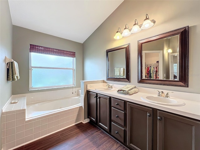 bathroom featuring vanity, wood-type flooring, tiled tub, and vaulted ceiling