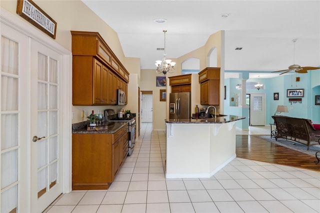 kitchen with stainless steel appliances, dark stone countertops, pendant lighting, ceiling fan with notable chandelier, and light wood-type flooring