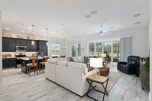 living room featuring ceiling fan with notable chandelier and light hardwood / wood-style flooring