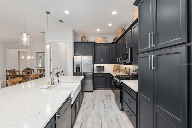 kitchen featuring appliances with stainless steel finishes, light stone counters, decorative light fixtures, light wood-type flooring, and a sink