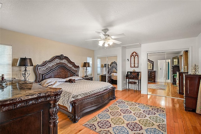 bedroom with multiple closets, ceiling fan, light hardwood / wood-style flooring, and a textured ceiling