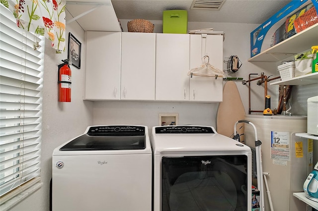 laundry area with cabinets, a textured ceiling, washer and clothes dryer, and water heater