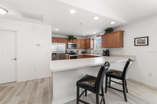 kitchen with stainless steel appliances, kitchen peninsula, light hardwood / wood-style floors, vaulted ceiling, and a breakfast bar area