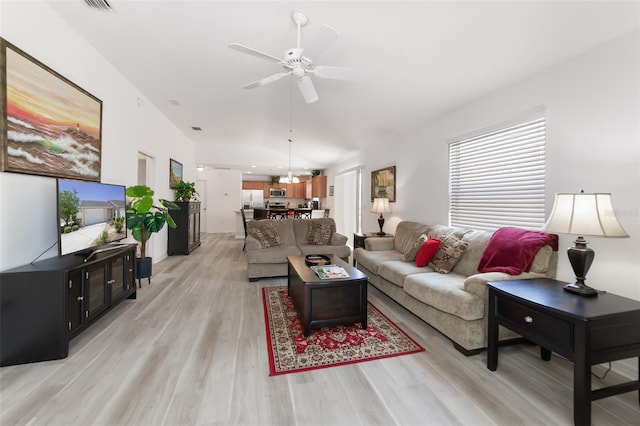 living room with ceiling fan with notable chandelier and light hardwood / wood-style flooring