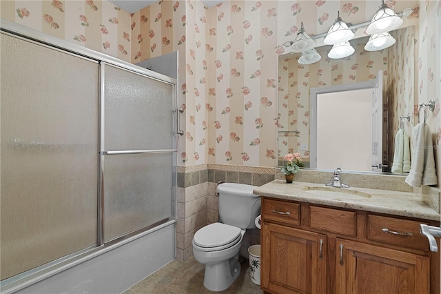 full bathroom with vanity, toilet, tile walls, and bath / shower combo with glass door