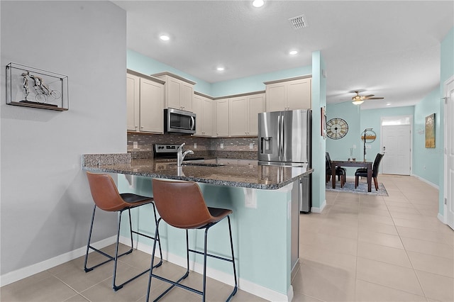 kitchen with kitchen peninsula, dark stone counters, decorative backsplash, a breakfast bar, and appliances with stainless steel finishes