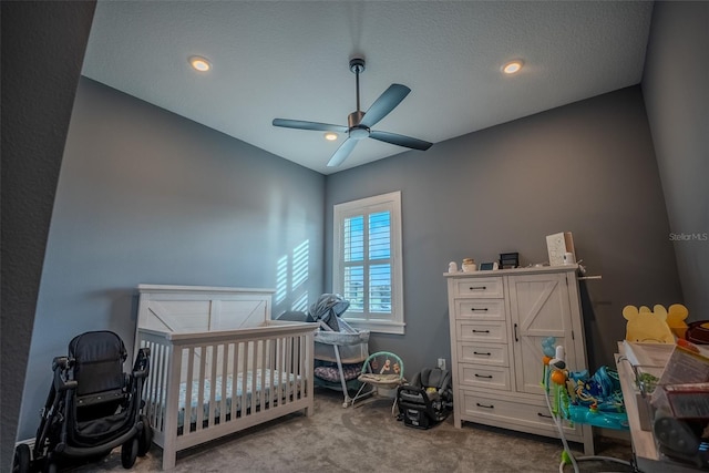 bedroom featuring a crib, light carpet, a textured ceiling, and ceiling fan