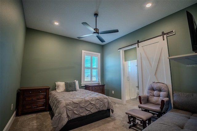 bedroom featuring light carpet, a barn door, ensuite bath, and ceiling fan