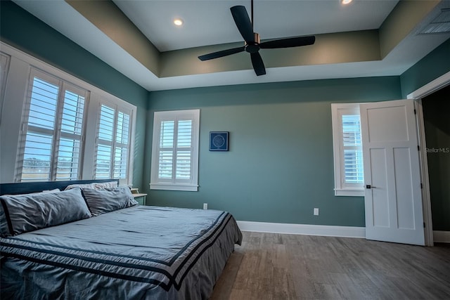 bedroom with hardwood / wood-style floors, ceiling fan, and a tray ceiling